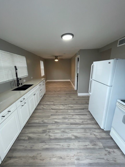 A white refrigerator is in a kitchen with wood flooring.