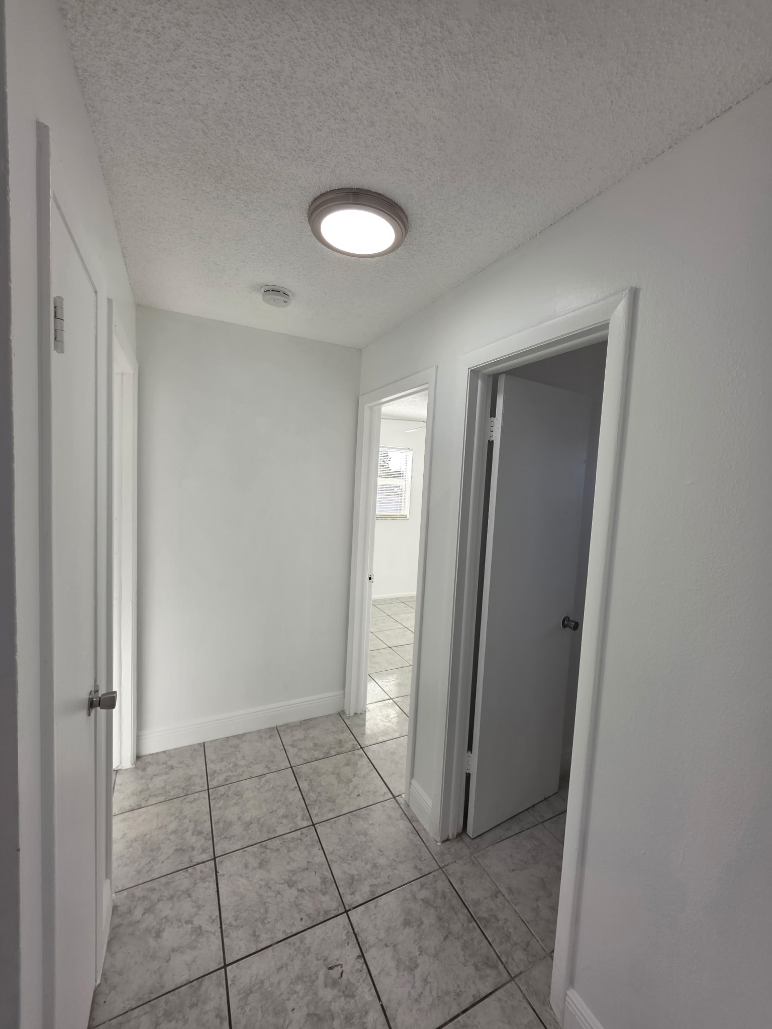 A white hallway with a tiled floor and a door on the right.