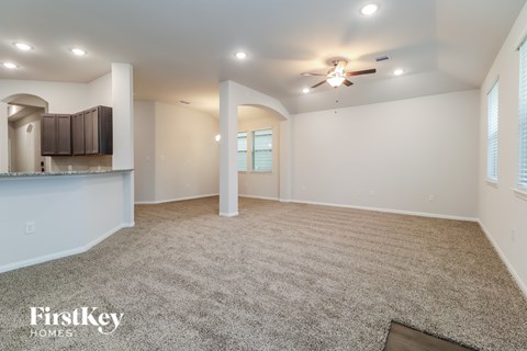 a living room with carpet and a kitchen with a ceiling fan