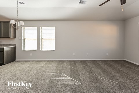 A spacious room with a carpet floor and a kitchen area to the left.