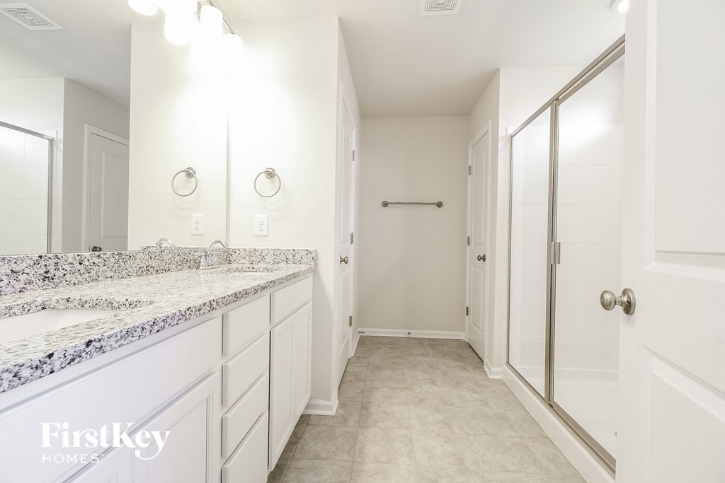 A white bathroom with a marble counter top and a walk in shower.