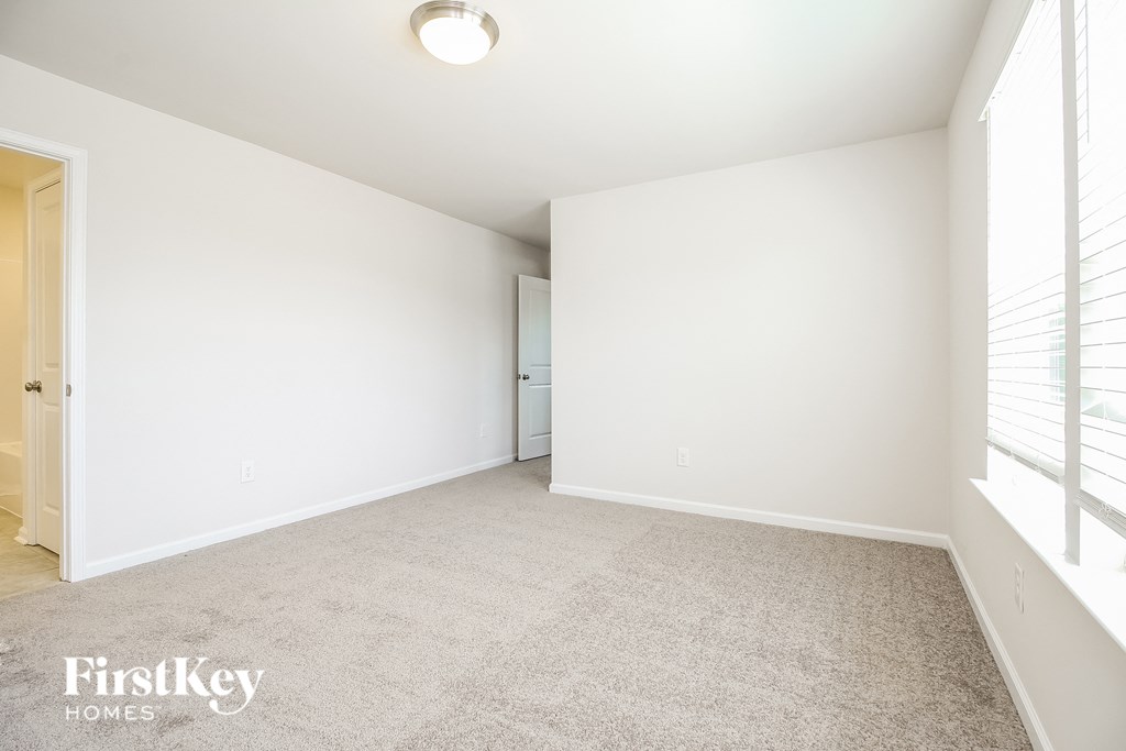 A spacious room with a carpeted floor and a window with blinds.