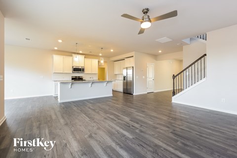 A spacious living room with a kitchen in the background and a staircase on the right.