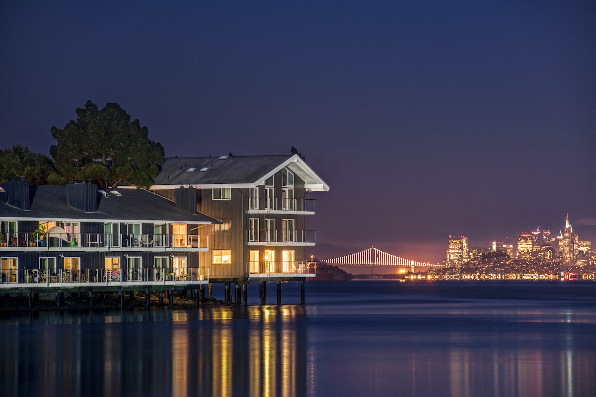 a house on the water at night with the skyline in the background