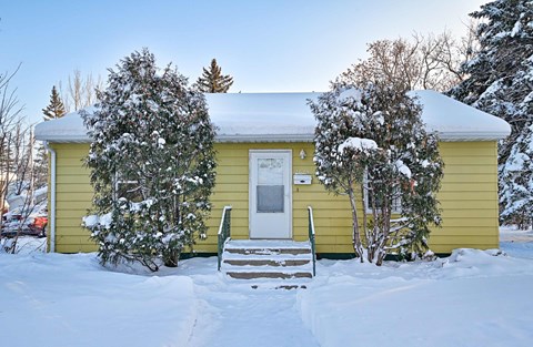 A yellow house with snow on the ground and trees.