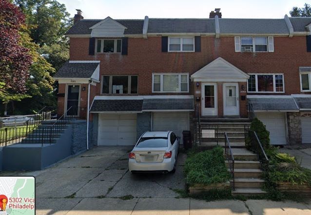 A two-story brick house with a car parked in front.