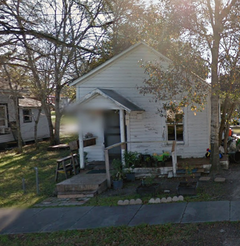 A small white house with a porch and a tree in front.