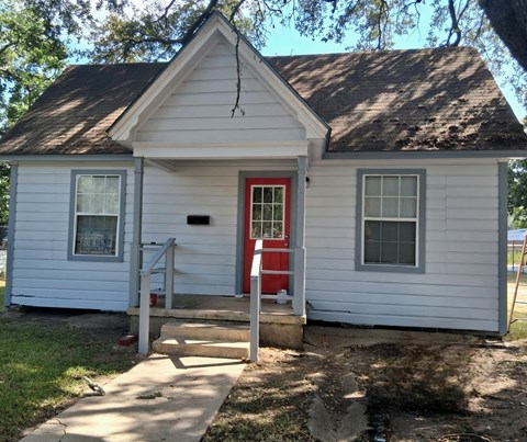 A small white house with a red door and a grey window.