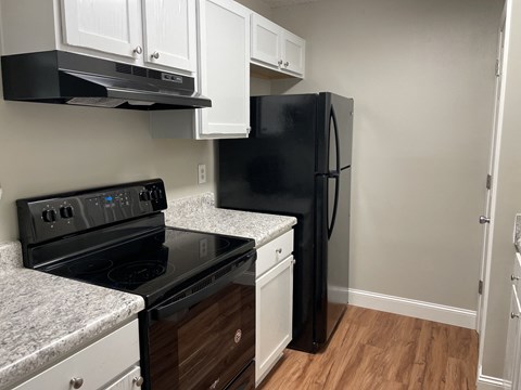 A black refrigerator is in a kitchen with white cabinets.