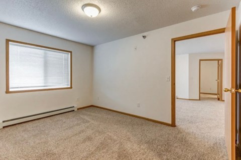 A room with a carpeted floor, a window with blinds, and a door.