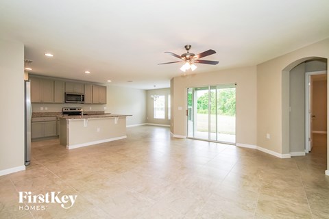 A spacious living room with a kitchen area in the background and a ceiling fan in the middle of the room.