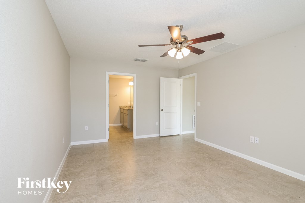 an empty living room with a ceiling fan and a hallway to a bathroom