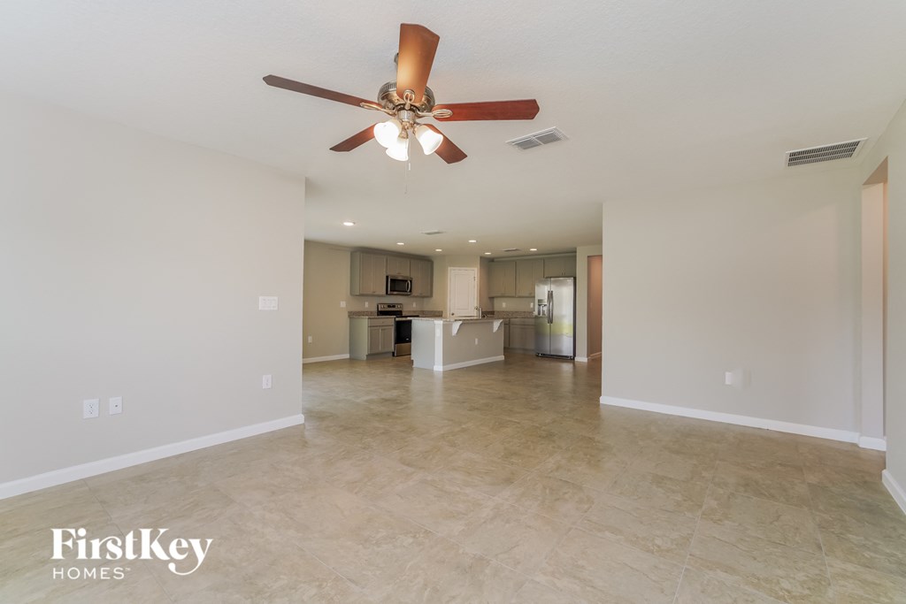 an empty living room with a ceiling fan and a kitchen