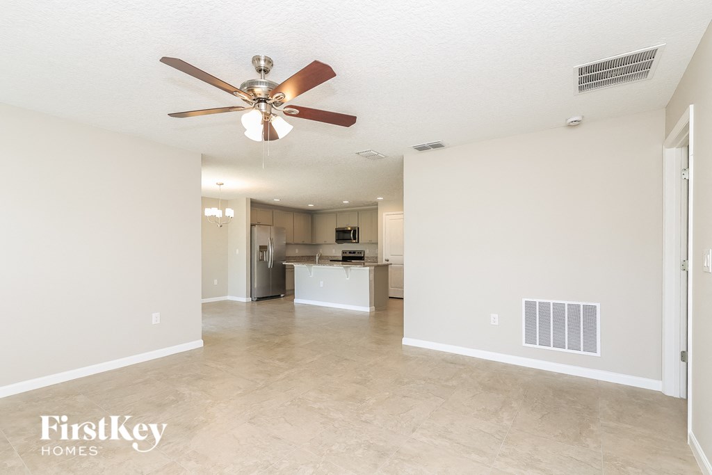 A spacious room with a ceiling fan and a kitchen area in the background.