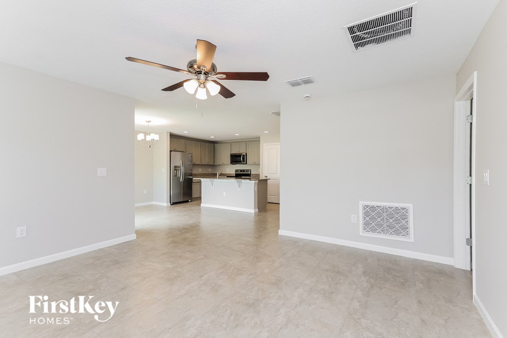 an empty living room with a ceiling fan and a kitchen