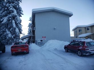 two cars parked in the snow in front of a garage