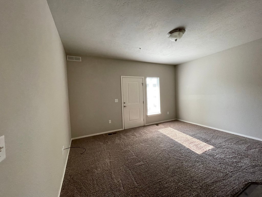 the living room of an empty apartment with carpet and a door