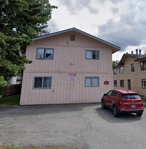 A red car is parked in front of a pink building with a sign on it.