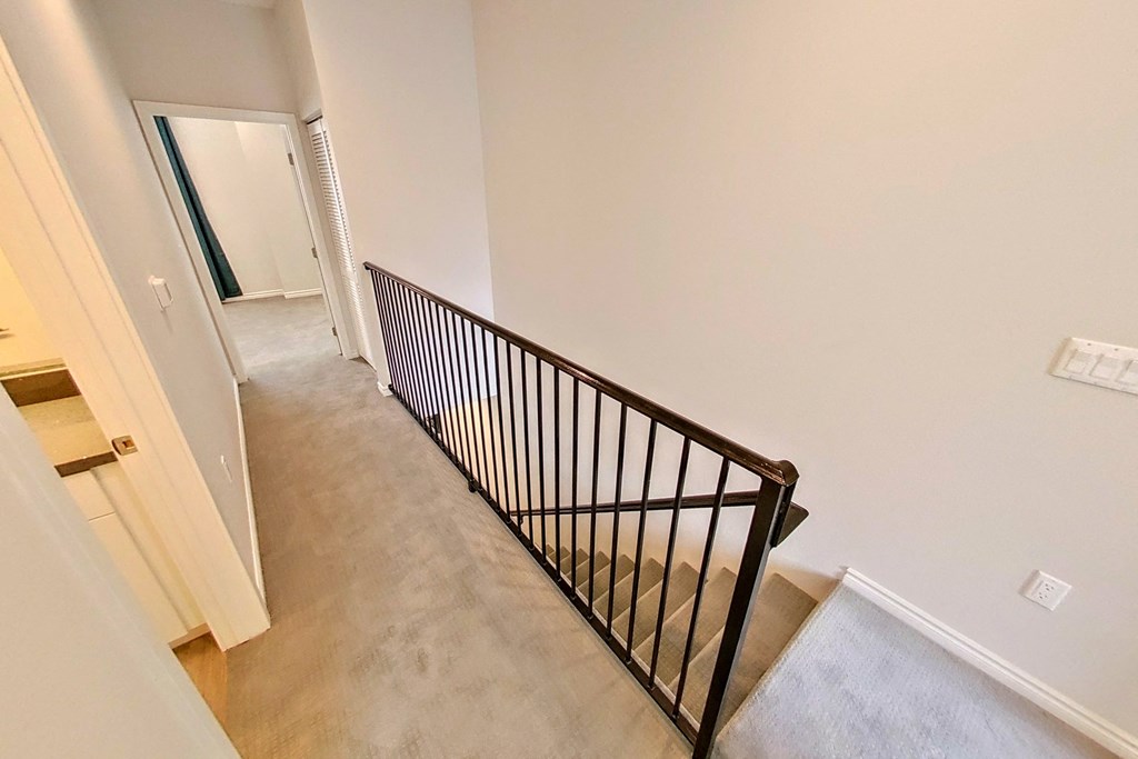 a stairway in a home with a railing and a hallway with a door to