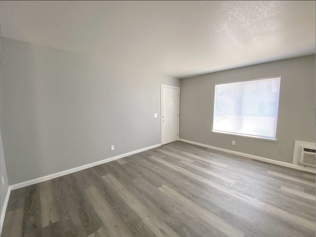 the living room of an empty home with wood floors and a window
