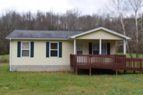 a small yellow house with a porch and a wooden deck