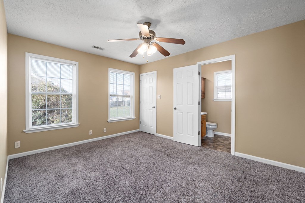 an empty living room with a ceiling fan and a door to a bathroom