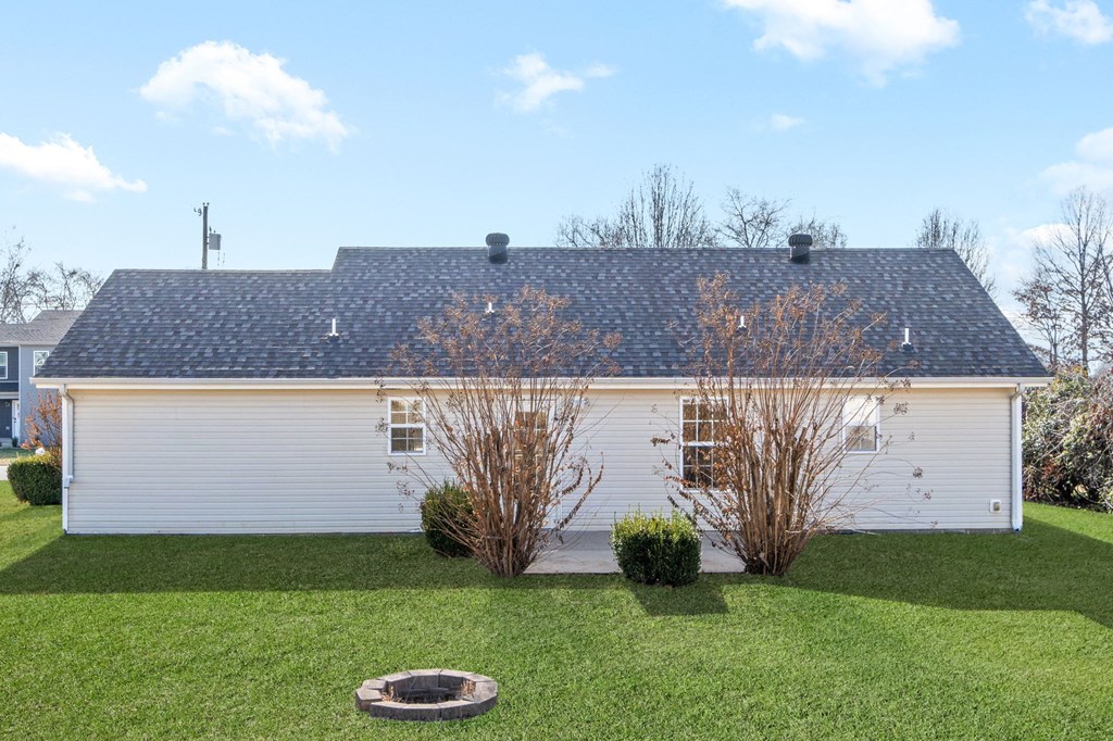 the backyard of a white house with a yard and a fire pit