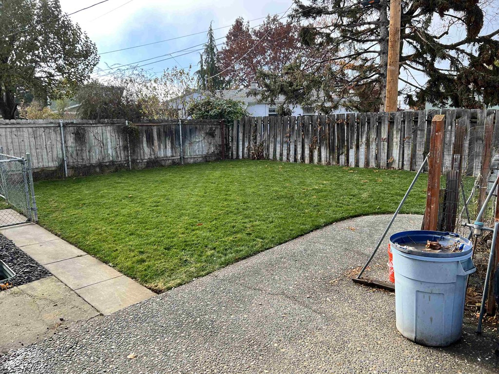 a backyard with a fence and a trash can