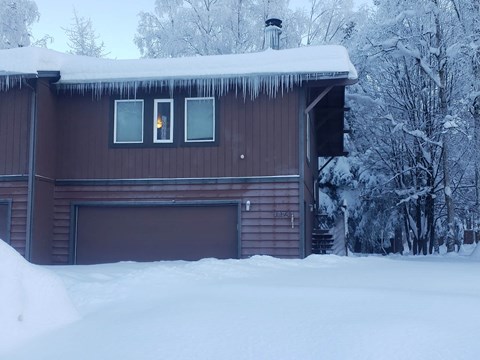 A house with snow on the roof and trees in the background.