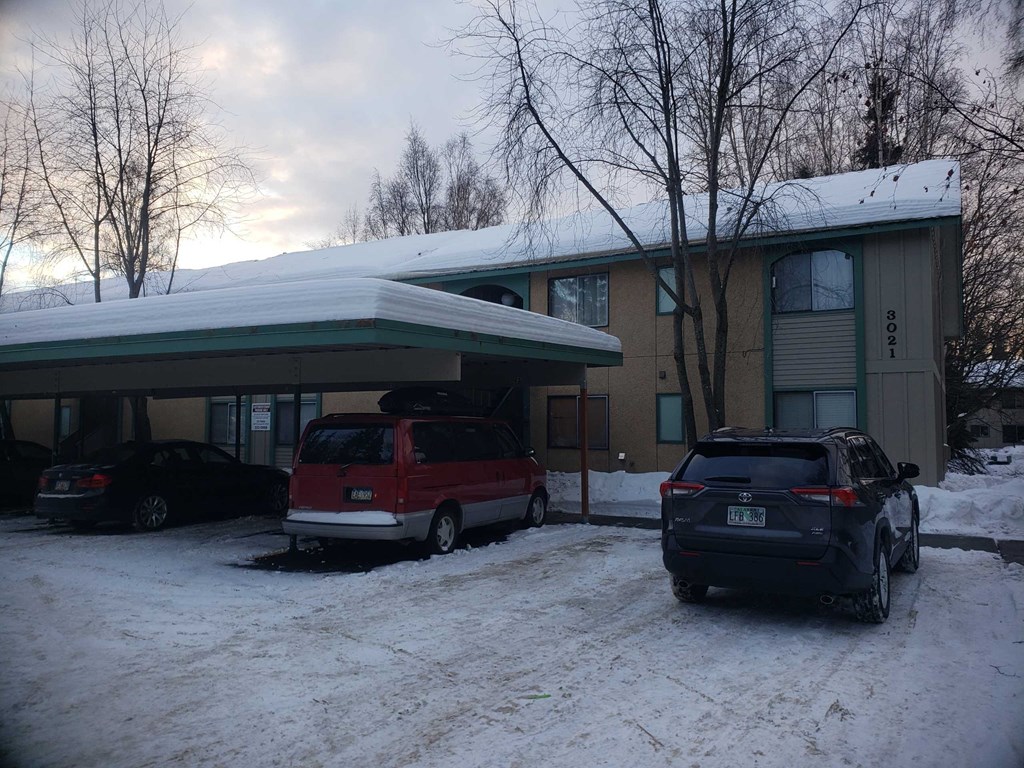 A red van is parked in front of a building with a black car to the right.
