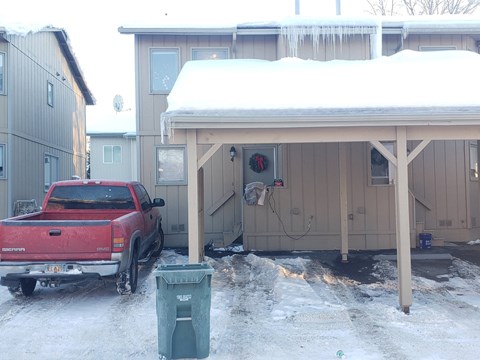 A red truck is parked in front of a house with a covered porch.