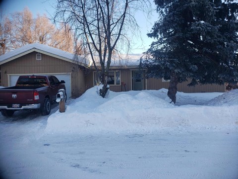 A snow-covered driveway with a truck parked in front of a house.