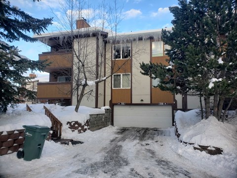 A snow-covered building with a green trash can in front.