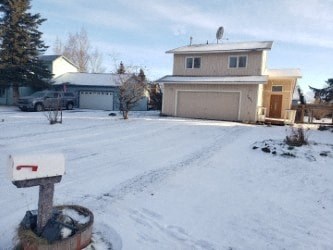 A mailbox sits on a snowy ground in front of a house.