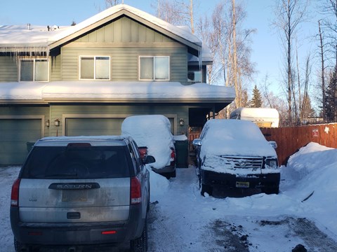 two cars parked in the snow in front of a house