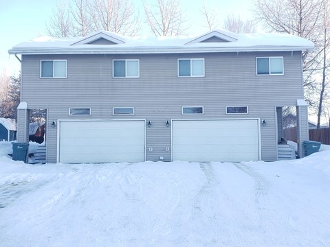 A grey house with two garages and a snow-covered driveway.