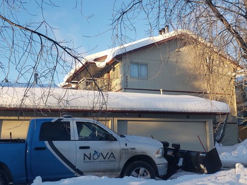 A Nova snow plow truck is parked in front of a house.