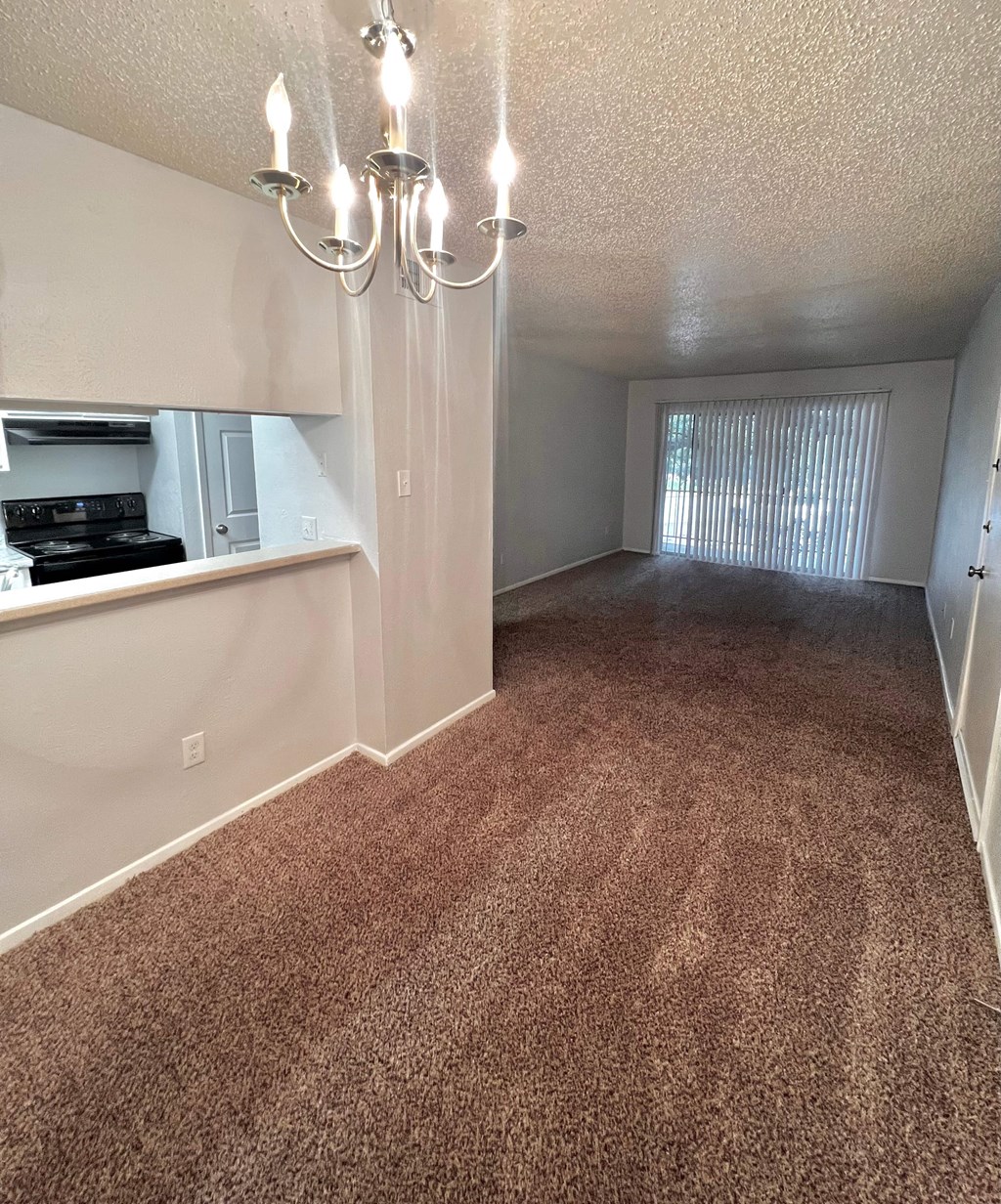 an empty living room with carpet and a kitchen
