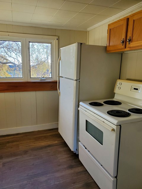 A white refrigerator and oven in a kitchen with wooden floors and a window.