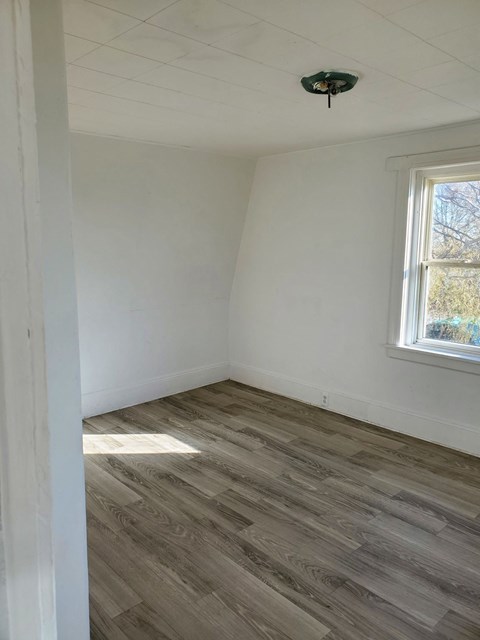 a room with white walls and wood flooring and a window
