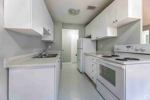 A white kitchen with a sink, stove, and refrigerator.