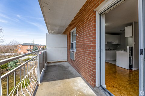 A balcony with a brick wall and a white door leading to a kitchen.