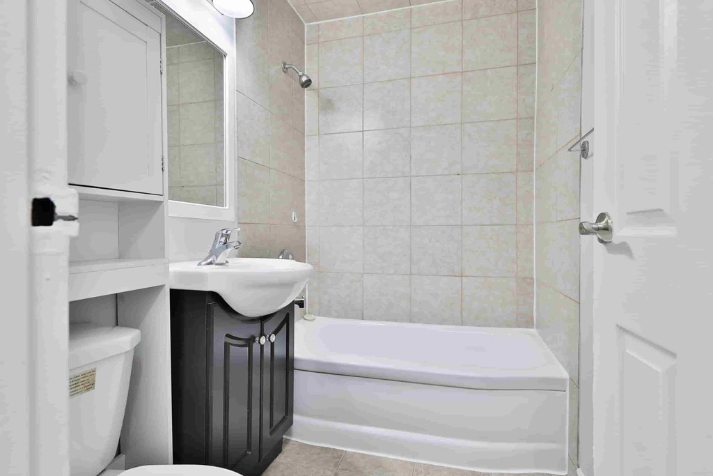 A white bathroom with a black trash can and a white sink.