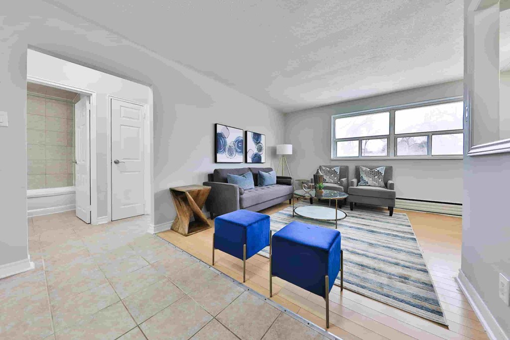 A living room with a grey couch, a blue ottoman, and a wooden coffee table.