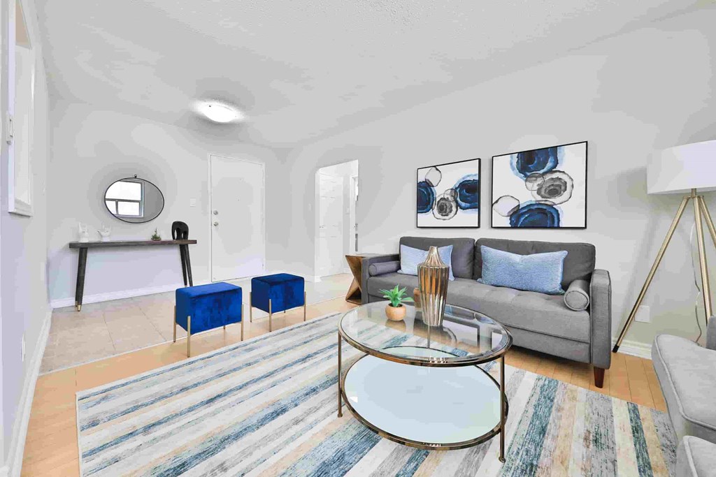 A living room with a grey couch, a glass coffee table, and a striped rug.