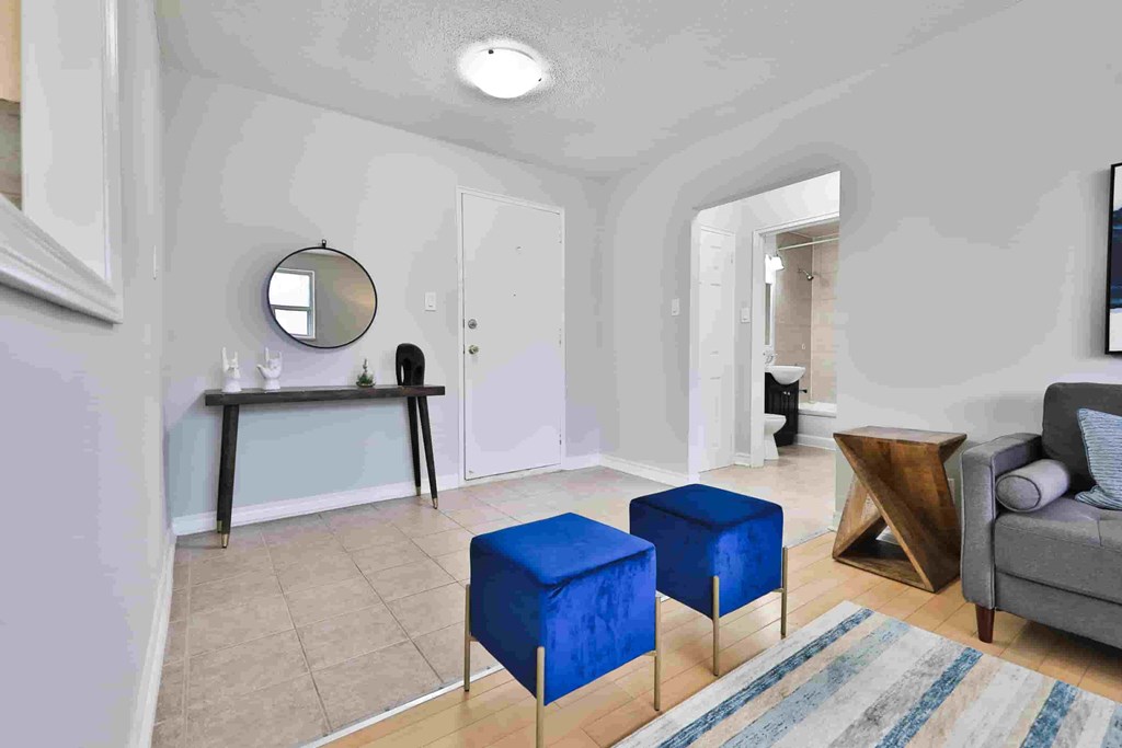 A living room with a grey couch, a mirror, a table, and two blue ottomans.