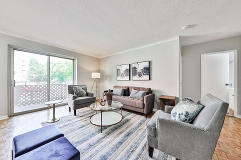 A living room with a grey couch, a blue ottoman, and a round glass table.