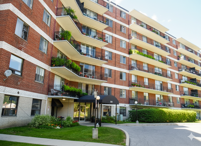 A red brick apartment building with balconies and plants.