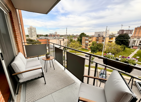 A balcony with a chair and table overlooking a cityscape.
