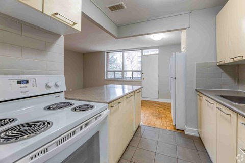 A white stove top oven sits in a kitchen with white cabinets and a window.
